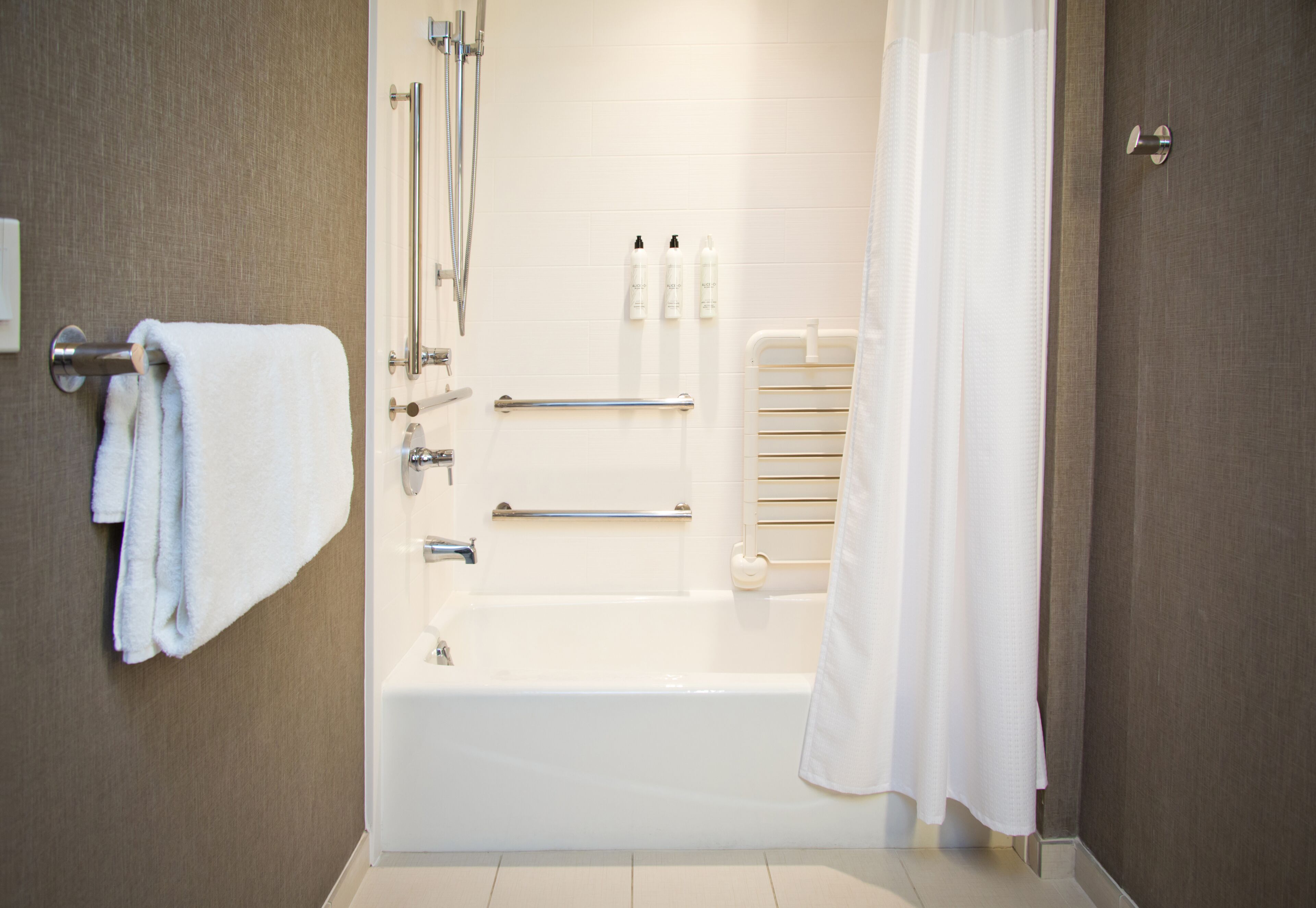 A modern bathroom with a bathtub, a towel rack, a handrail, and a shower curtain.