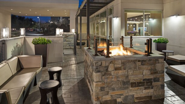 Un patio exterior con asientos de piedra, una fogata y un área acristalada con iluminación interior.