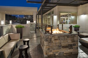 An outdoor patio with stone seating, a fire feature, and a glass-enclosed area with interior lighting. - SpringHill Suites by Marriott West Sacramento (West Sacramento)