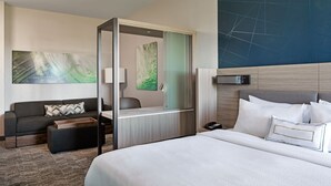 Una habitación de hotel moderna con una cama grande, un sofá, un escritorio y un separador de vidrio.