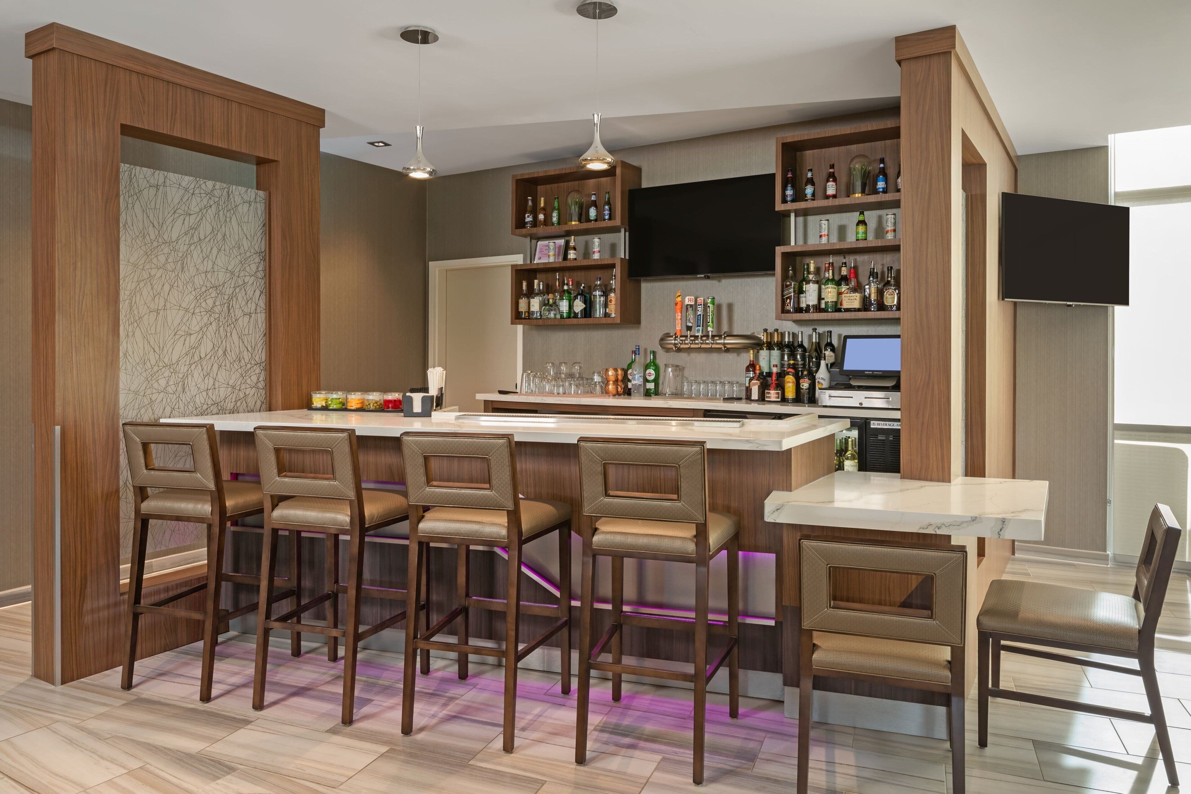 A modern kitchen with a bar area, wooden cabinets, and a flat-screen TV.