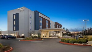 Un hotel moderno con un llamativo letrero de 'SPRINGHILL SUITES', un amplio estacionamiento y una entrada bien iluminada.