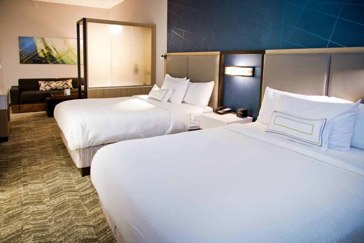 A hotel room with two beds, a sofa, a desk, and a large window.
