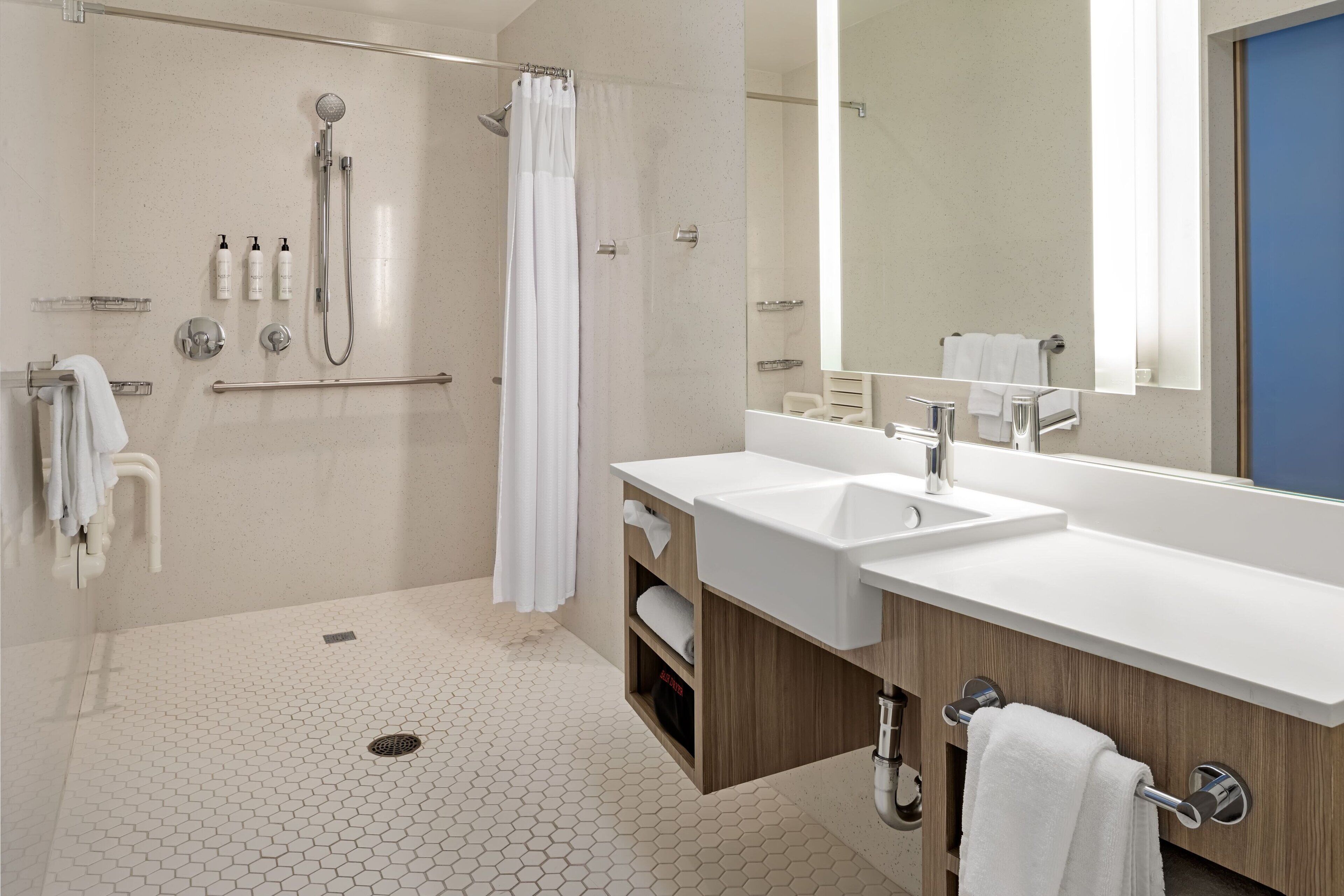 A modern bathroom with a shower, two sinks, a large mirror, and a wooden vanity.