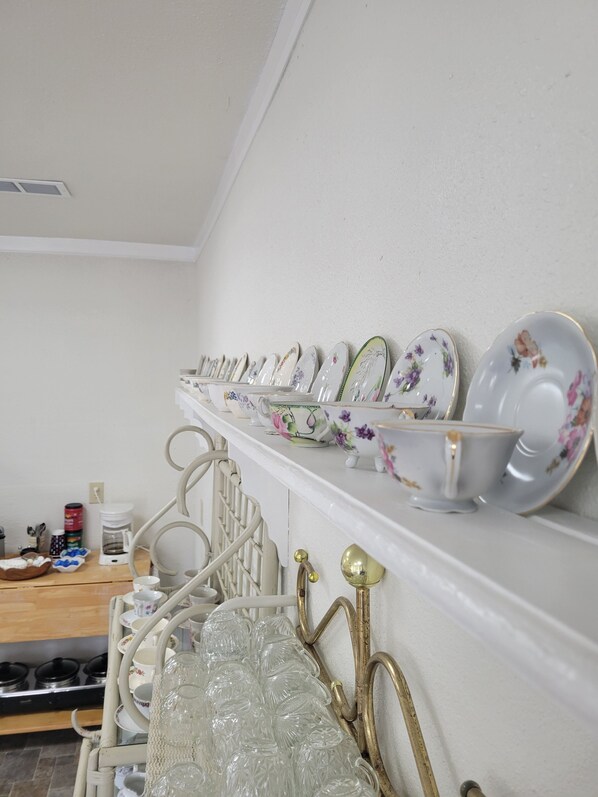 Una cucina con un piano di lavoro bianco, una macchina da caffè e un espositore per piatti e bicchieri.