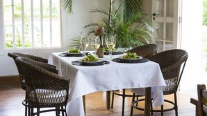 Un comedor con mantel blanco, sillas de mimbre y una planta grande en maceta.