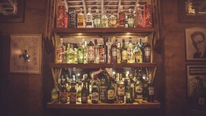 Un bar con múltiples estantes llenos de botellas de licor, cuadros en las paredes y un cartel sobre los estantes.