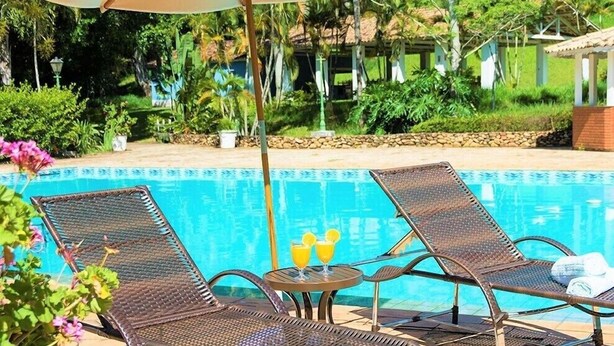 Un área junto a la piscina con sillas de descanso, una mesa con bebidas y una sombrilla grande.