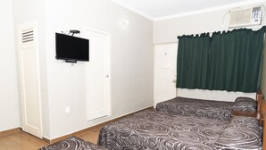 Una habitación con dos camas, un televisor montado en la pared, una puerta y una ventana con cortina verde.