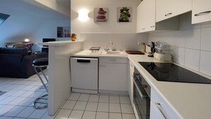 Una cucina compatta con mobili bianchi, lavastoviglie, piano cottura e lavello. C'è un piccolo angolo ristoro con tavolo e sedie.