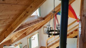 Habitación estilo loft con techo de madera, una hamaca colgante, un sofá blanco y una escalera que conduce a un nivel superior.