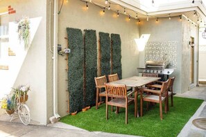 An outdoor patio with a wooden table and chairs, a grill, and vertical greenery. - Darcy's Beach House: Beach, Boardwalk & Pet Friendly! (Wildwood)