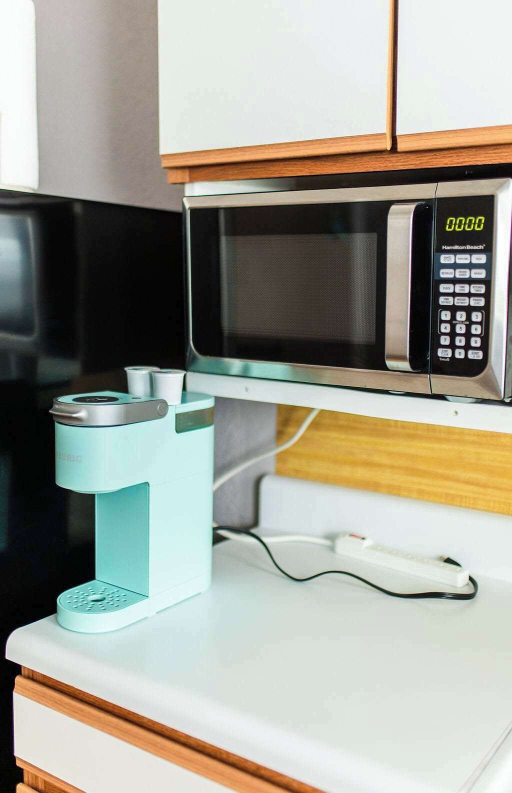 A kitchen with a microwave, a coffee machine, and a white countertop.