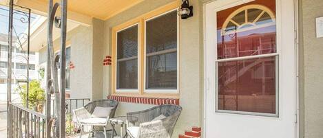 A covered porch with wicker furniture, a white door, and a window with a view.