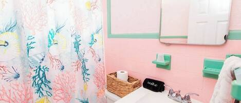 A bathroom with a pink wall, a white sink, a mirror, a green towel rack, and a shower curtain with a coral pattern.