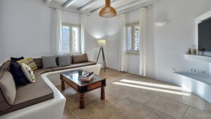 A modern living room with a sectional sofa, a coffee table, and a floor lamp. There are large windows with curtains, a flat-screen TV mounted on the wall, and a stone fireplace. - Villa Leo, 3km From the Paroikia With a Nice View of the Paroikia and Port (Paros)
