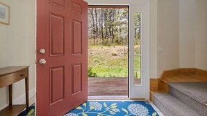 A room with a red door, a wooden bench, and a view of a grassy area with trees.