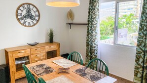 A dining area with a wooden table, green chairs, a clock, a lamp, and a window with curtains. - Suite Natura @ Casa del Lago (Puerto de la Cruz)