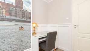 Una habitación con escritorio, silla y vista a un río con barcos.