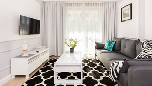 Una sala de estar moderna con un televisor de pantalla plana, una mesa de centro blanca, un sofá gris con cojines estampados y una alfombra en blanco y negro.