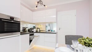 Una cocina moderna con armarios blancos, horno empotrado y zona de comedor con mesa para dos.