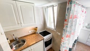 Une cuisine de taille réduite avec des armoires blanches, un plan de travail en granit, une cuisinière, un évier et une fenêtre.