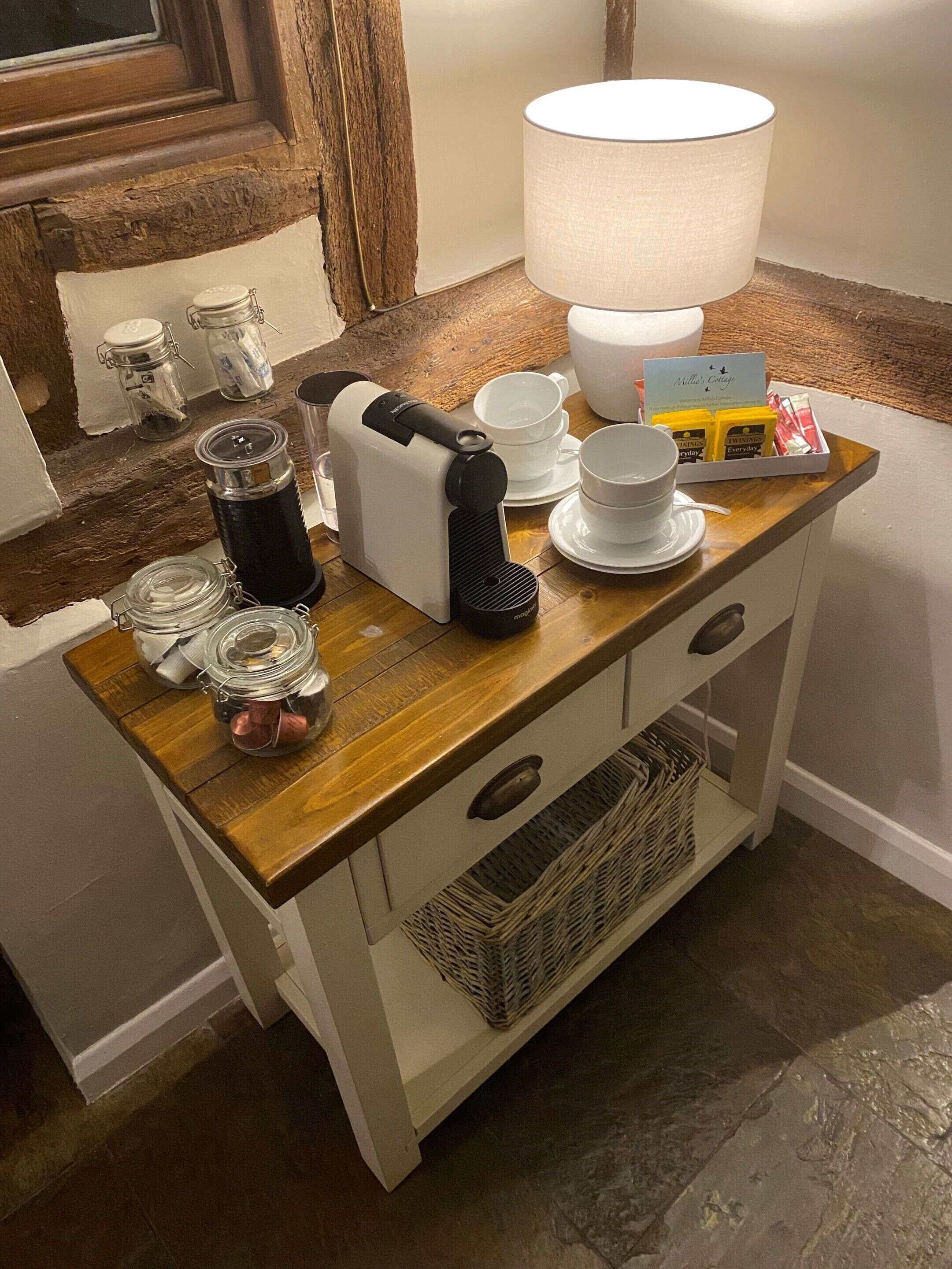 A kitchenette with a coffee maker, jars, a lamp, and a tray with Twinings tea bags.