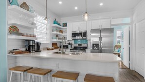 A modern kitchen with white cabinetry, stainless steel appliances, and a central island with bar stools. - Palm Place, Spacious beach house steps to the powdery sand and emerald water. (Destin)