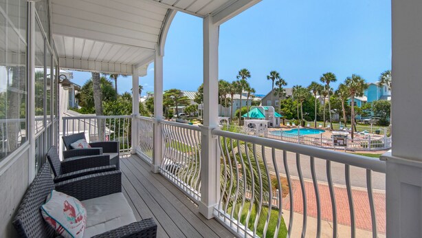 A covered outdoor area with wicker furniture and a view of a swimming pool and buildings. - Palm Place, Spacious beach house steps to the powdery sand and emerald water. (Destin)