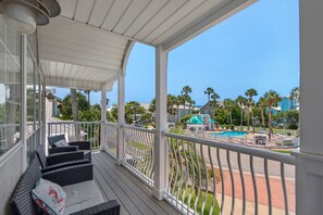 A covered outdoor area with wicker furniture and a view of a swimming pool and buildings. - Palm Place, Spacious beach house steps to the powdery sand and emerald water. (Destin)