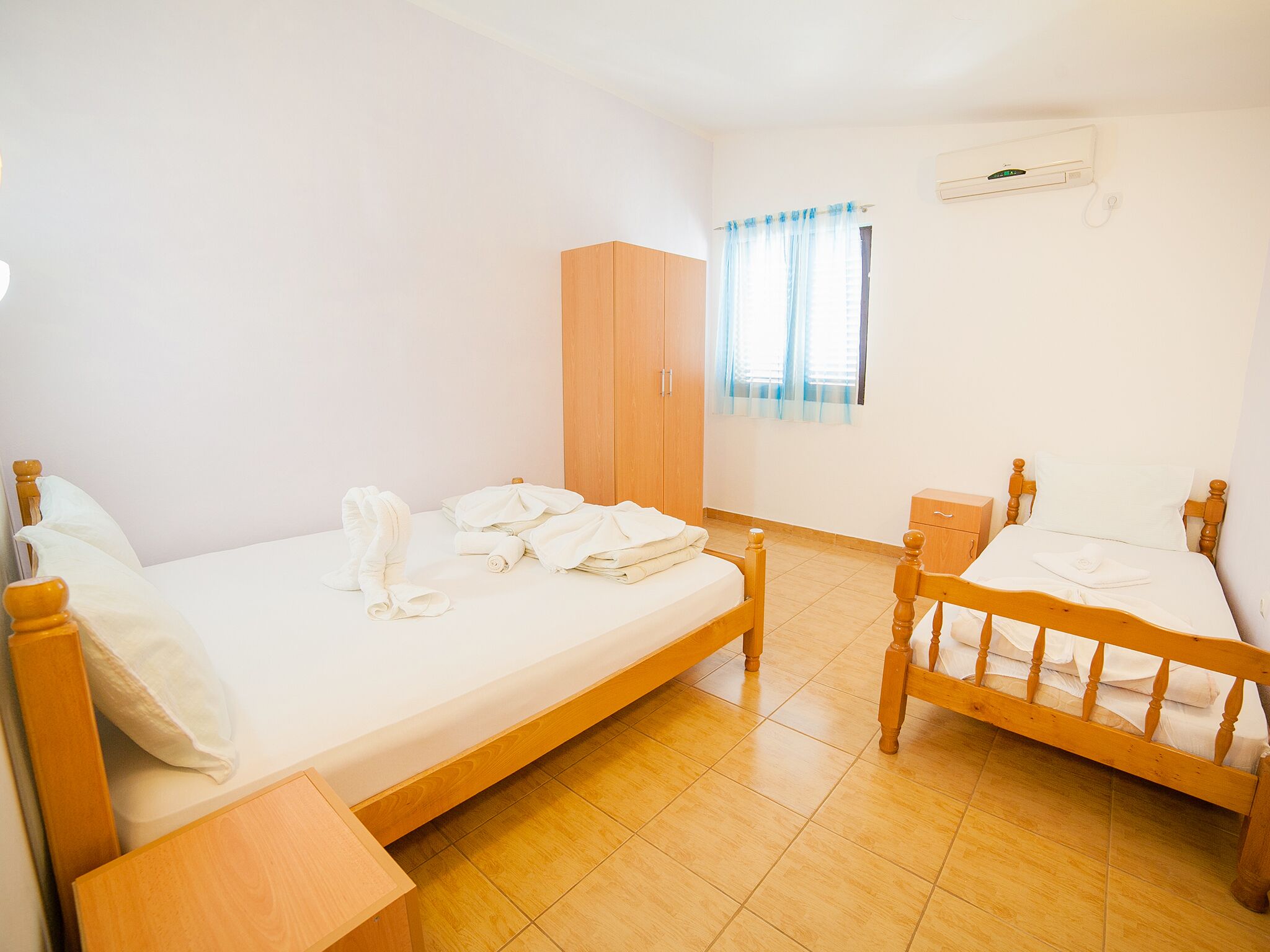 Ein Zimmer mit zwei hölzernen Betten, einem Schrank und einem Fenster mit Vorhängen.