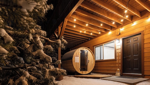 A wooden cabin with a snow-covered ground, a wooden sauna, and a door with a warning sign.