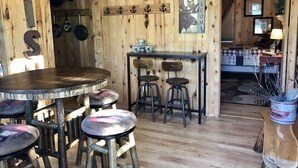 Un intérieur rustique en bois, avec une table ronde en bois, quatre tabourets et un coin bar.