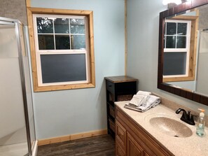 Un baño con ventana de madera, un lavabo con dispensador de jabón y un espejo sobre el lavabo.