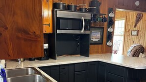 Une cuisine avec des meubles de couleur sombre, un plan de travail en marbre, un four à micro-ondes encastré et une machine à café.