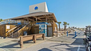 A beachside building with a wooden deck, a staircase leading to a covered area, and a vending machine labeled "BAGGED ICE". - Sandpiper Unit 4209/Beach Service/Gated Cmty/Reserved Parking/Many Amenities!!!! (Destin)