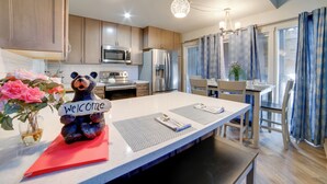 Cozinha moderna com armários de madeira, eletrodomésticos de aço inoxidável e uma ilha central com uma figura de urso segurando uma placa de 'Welcome'.