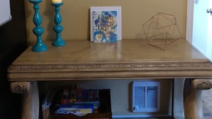 Una mesa con un cuadro de una flor, dos velas, un cuaderno y un objeto geométrico.