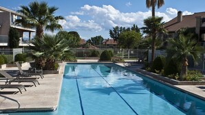 Une piscine rectangulaire à l’eau d’un bleu cristallin, entourée d’une clôture blanche et de palmiers.