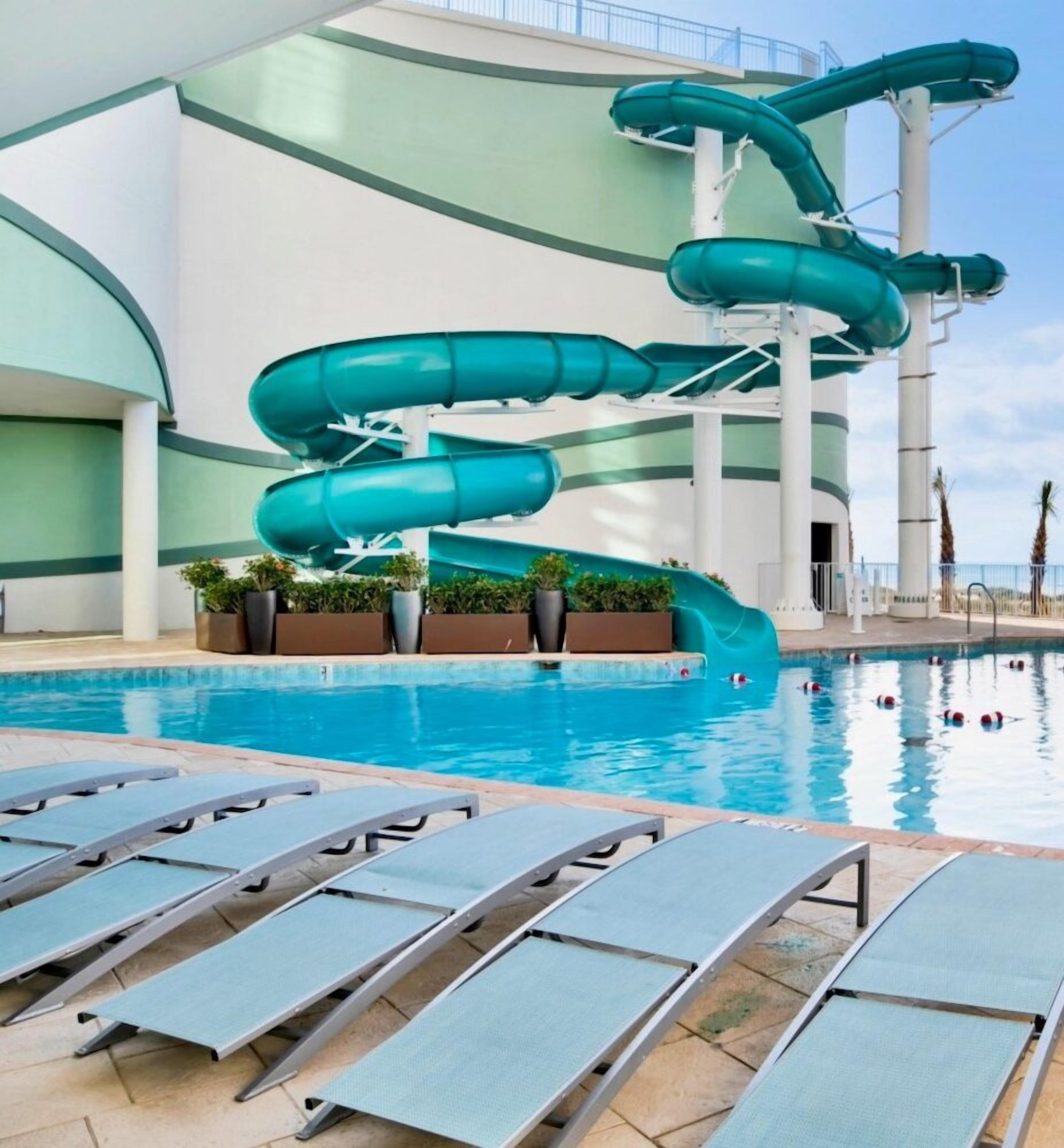 Una piscina con tobogán de agua, sillas de descanso y palmeras.