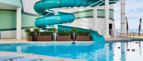 Una piscina con tobogán de agua, sillas de descanso y palmeras.