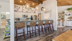 A modern kitchen with a central island, bar stools, hanging light fixtures, and nautical-themed decor. - Recovery Room | 300 ft from the beach | Private Pool, Hot Tub, Dog Friendly (Virginia Beach)