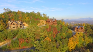 A large, multi-story wooden lodge with a prominent balcony, surrounded by a forested hillside.