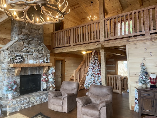 A cozy cabin interior with a stone fireplace, leather armchairs, a Christmas tree, and a wooden balcony. - Selah View  Stunning 5 BR mountain lodge - Incredible views, 3mi to Pigeon Forge (Sevierville)