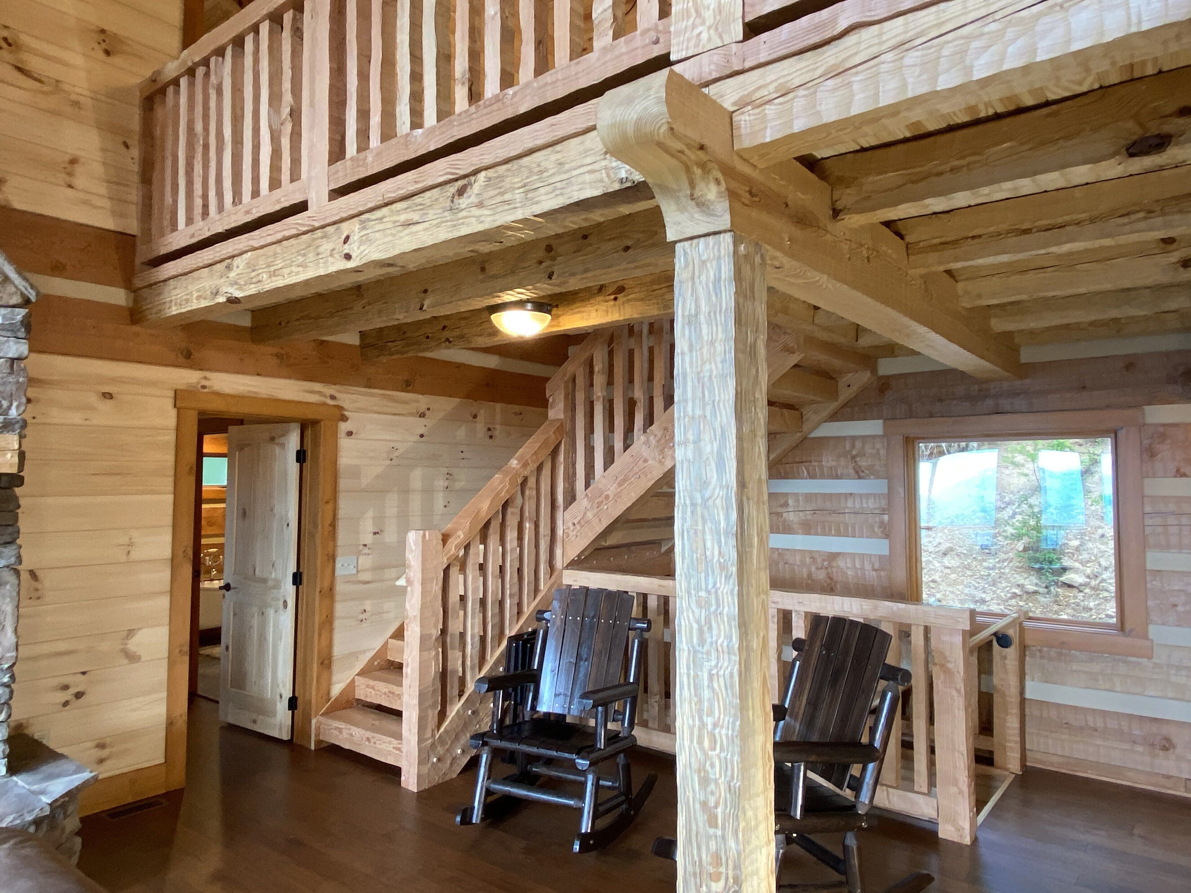 L’intérieur d’un chalet en bois, avec un escalier, deux fauteuils à bascule et un mur en pierre.