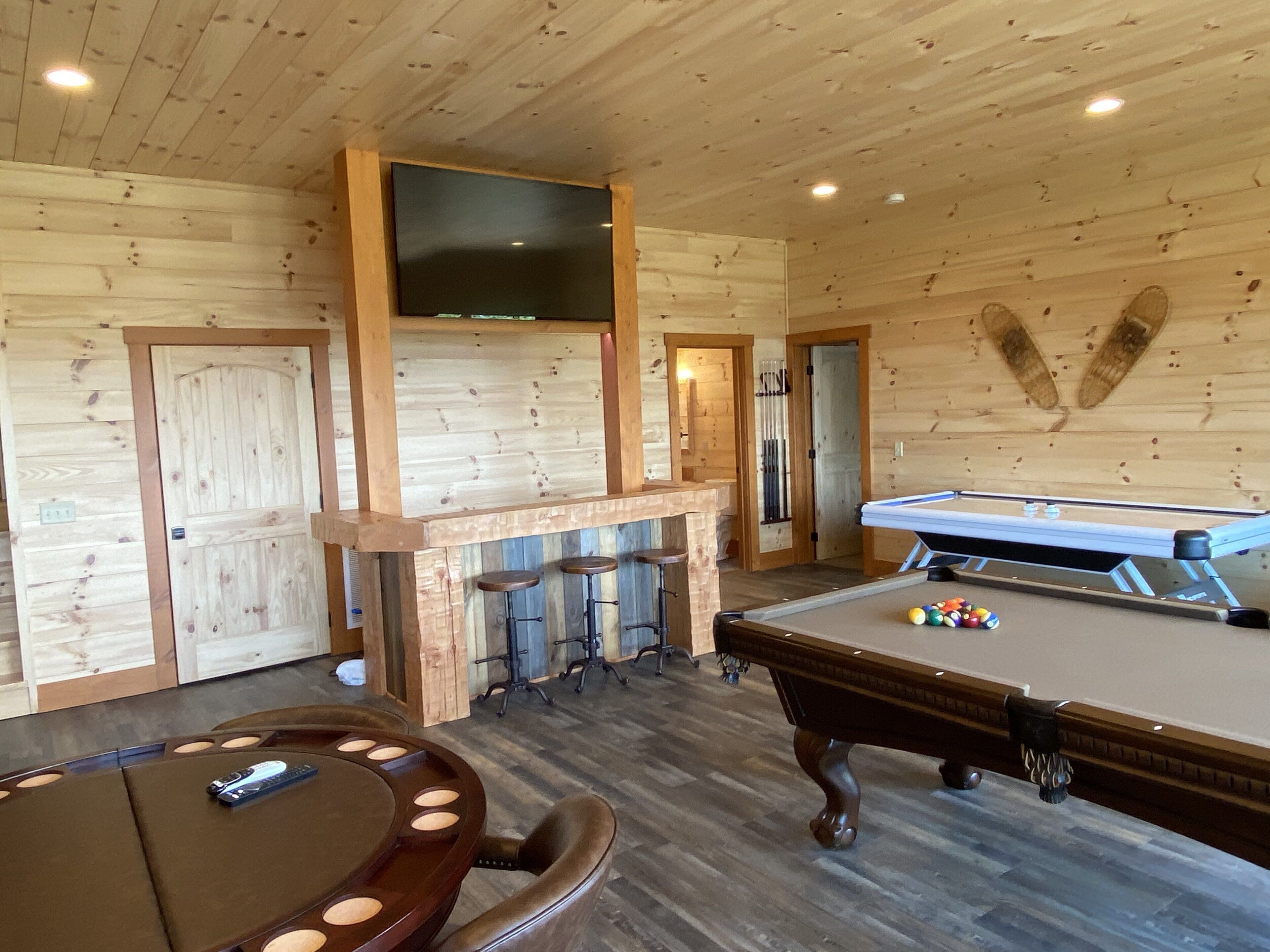 A wooden room with a pool table, bar area, and seating.