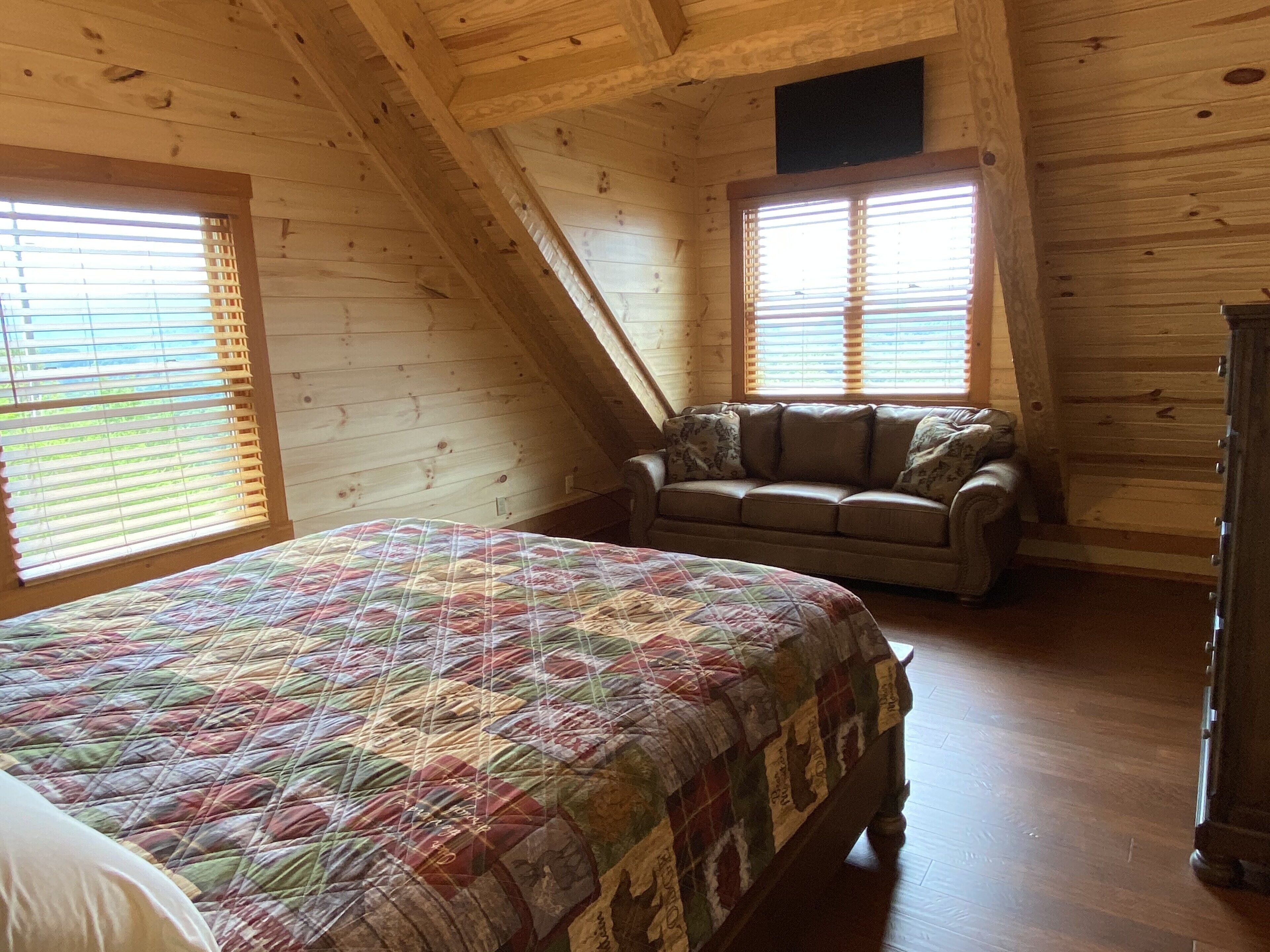 A cozy attic bedroom with a large bed, a sofa, and wooden walls.