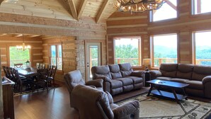 A spacious living room with a fireplace, large windows, and a dining area with a table and chairs.