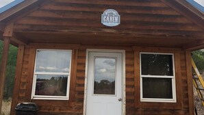 Une cabane en bois avec une pancarte indiquant « Bienvenue », une porte d’entrée et deux fenêtres.
