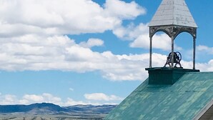 Une église dotée d’un clocher et d’une croix, entourée de chevaux et se dressant au milieu d’un paysage montagneux.
